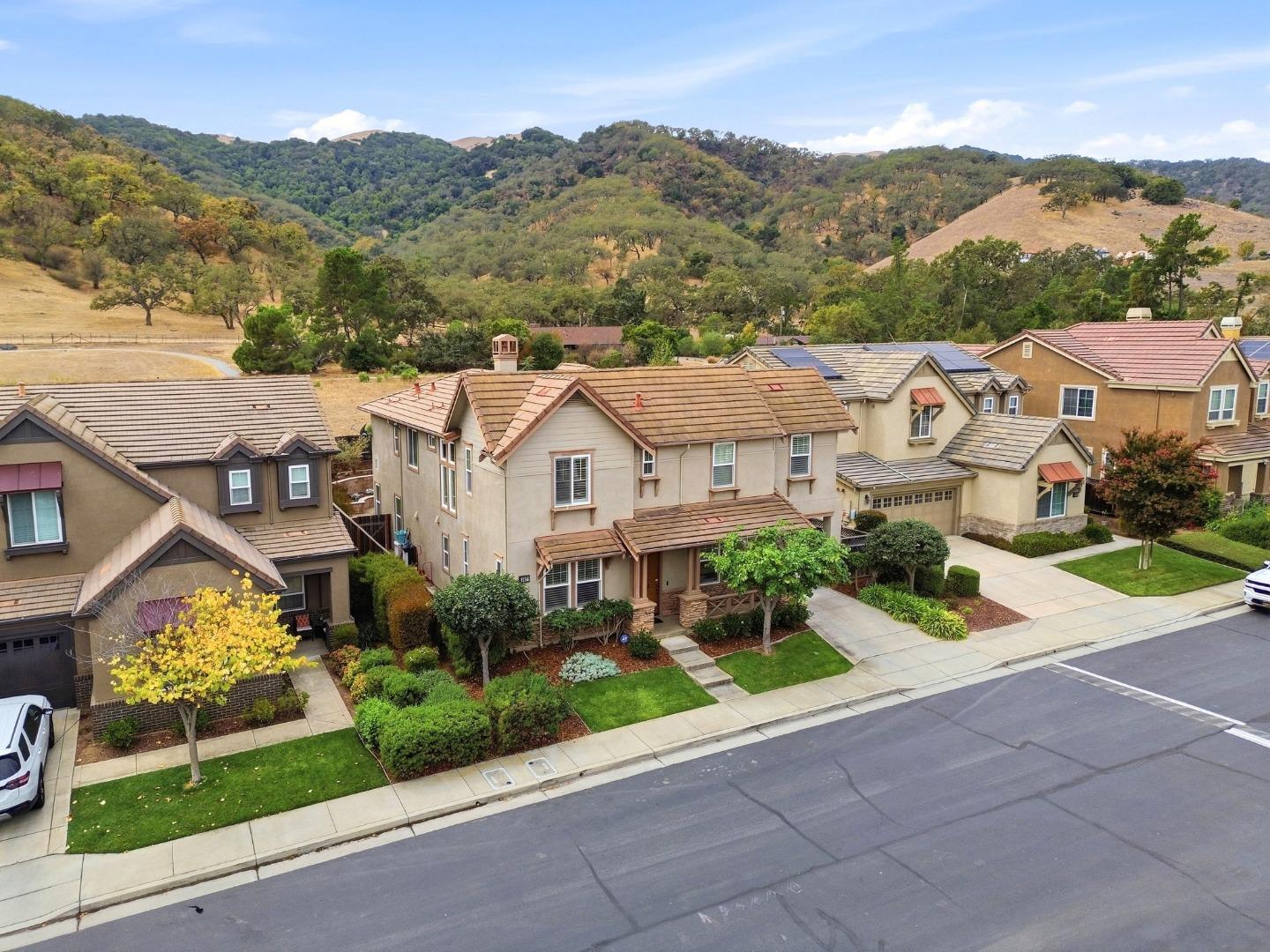 Two-story home on a residential street, with landscaped yards and rolling hills in the background.