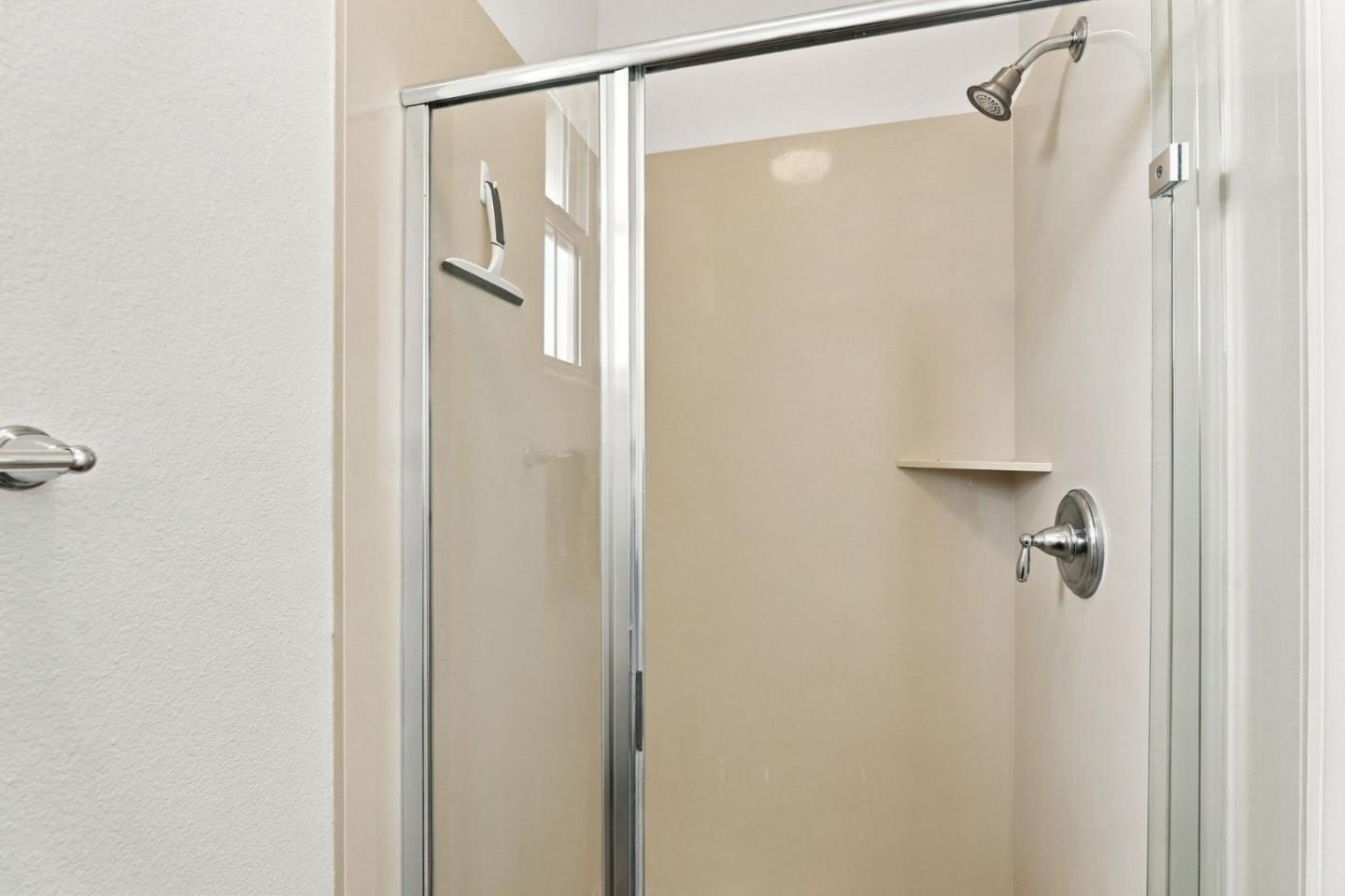 Beige shower stall with a glass enclosure, chrome fixtures, and a built-in shelf.