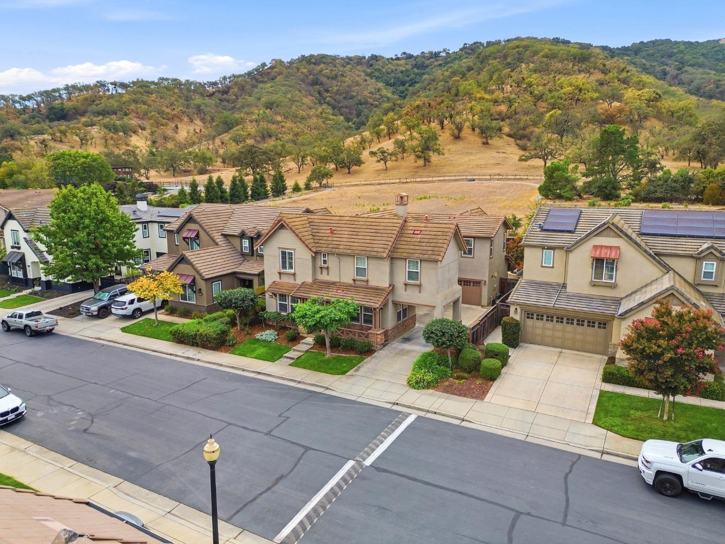 Aerial view of a tan two-story home on a residential street, with rolling hills behind it.