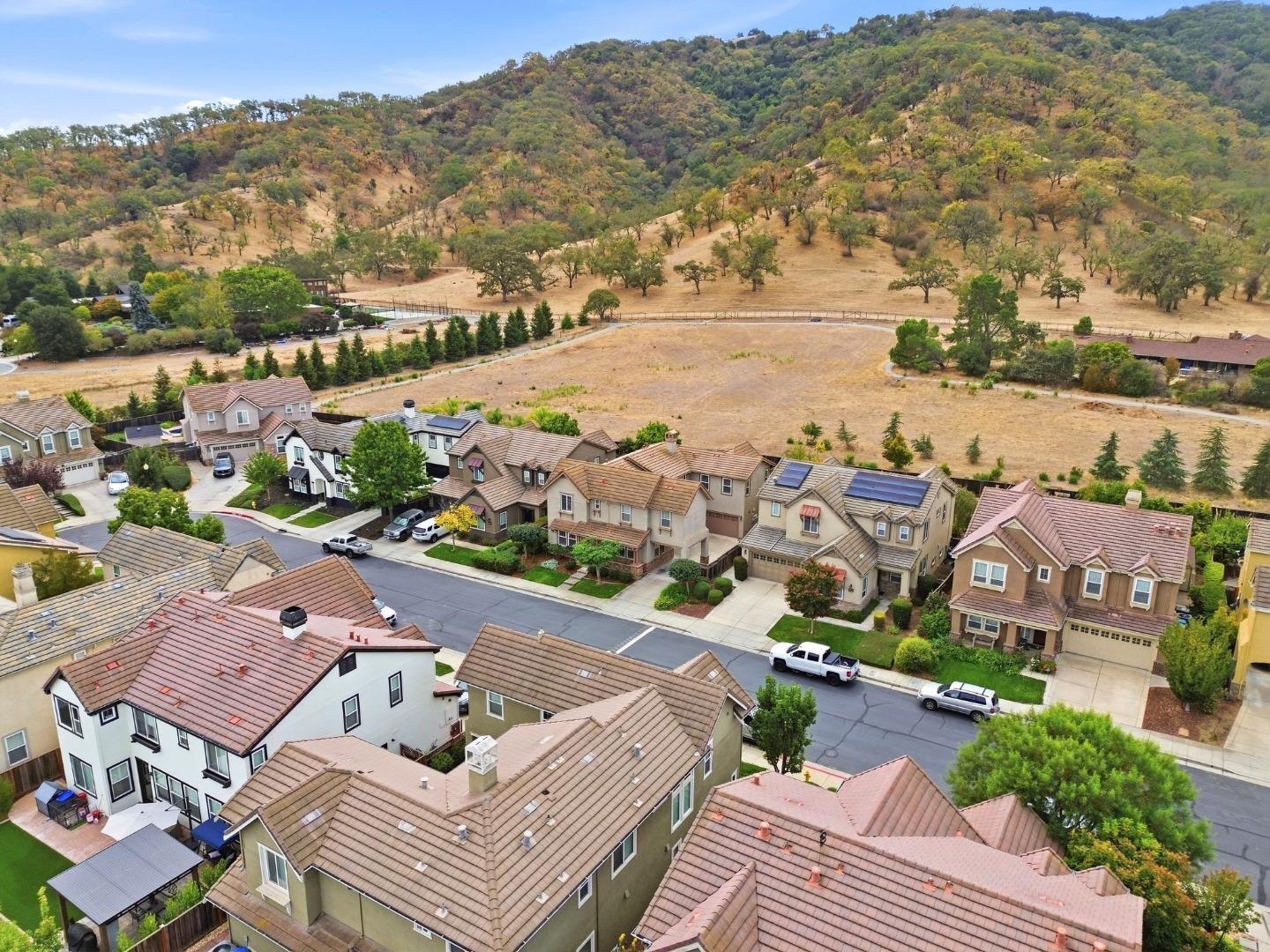 Aerial view of homes beside a dry open field, with wooded hills in the background.