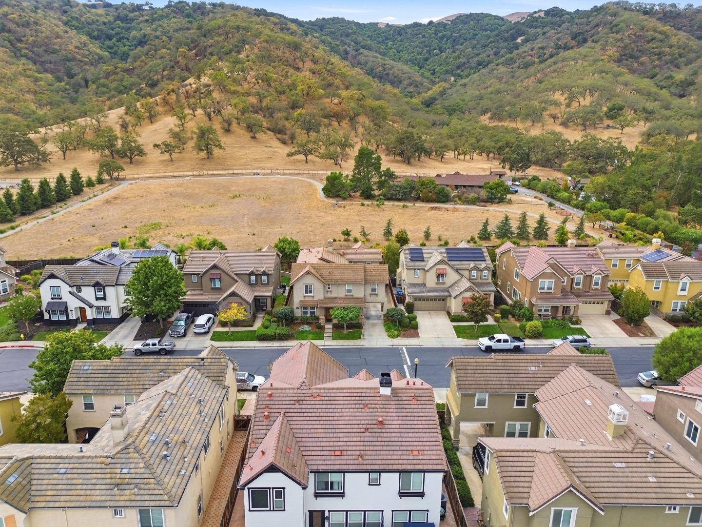 Aerial view of neighborhood homes beside an open hillside and wooded ridges.