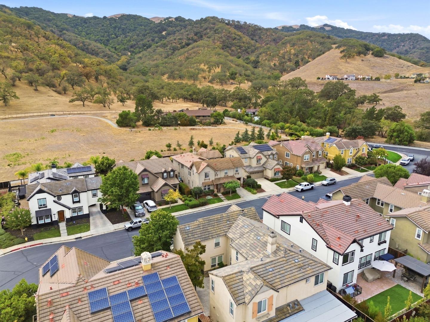 Aerial view of homes with solar panels beside rolling, tree-covered hills.