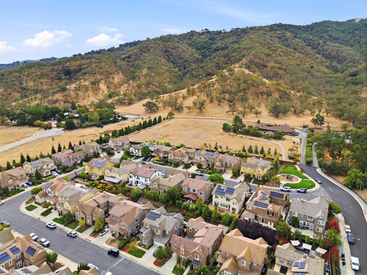 Aerial view of homes beside dry, tree-covered rolling hills.
