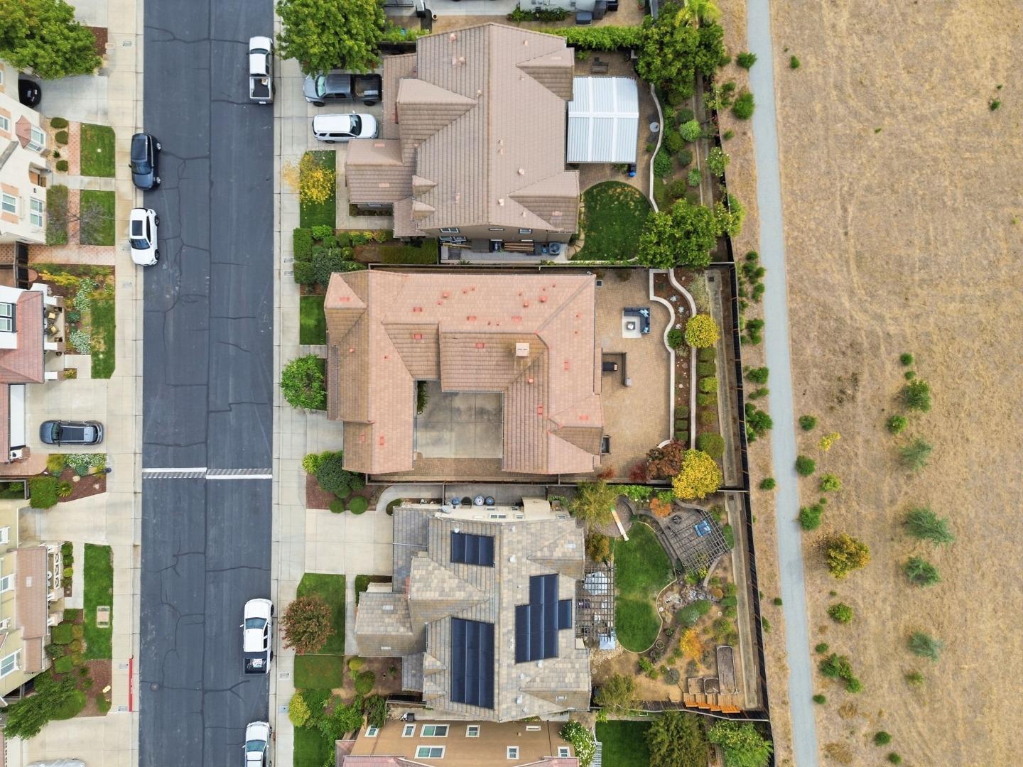 Aerial view of a tiled-roof home with an enclosed patio, landscaped yard, and neighboring dry field.