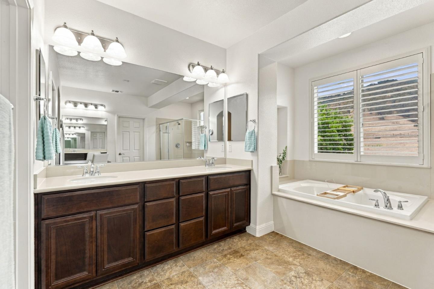 Bathroom with a dark wood double vanity and soaking tub beneath a shuttered window.