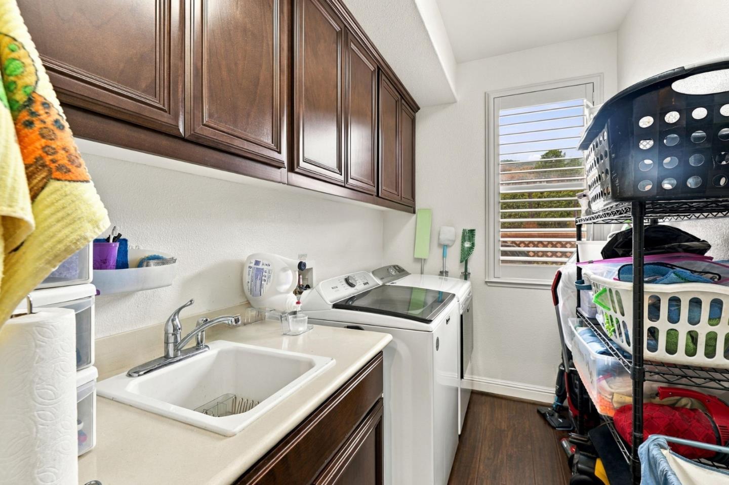Laundry room with dark wood cabinets, utility sink, washer and dryer, and storage racks.