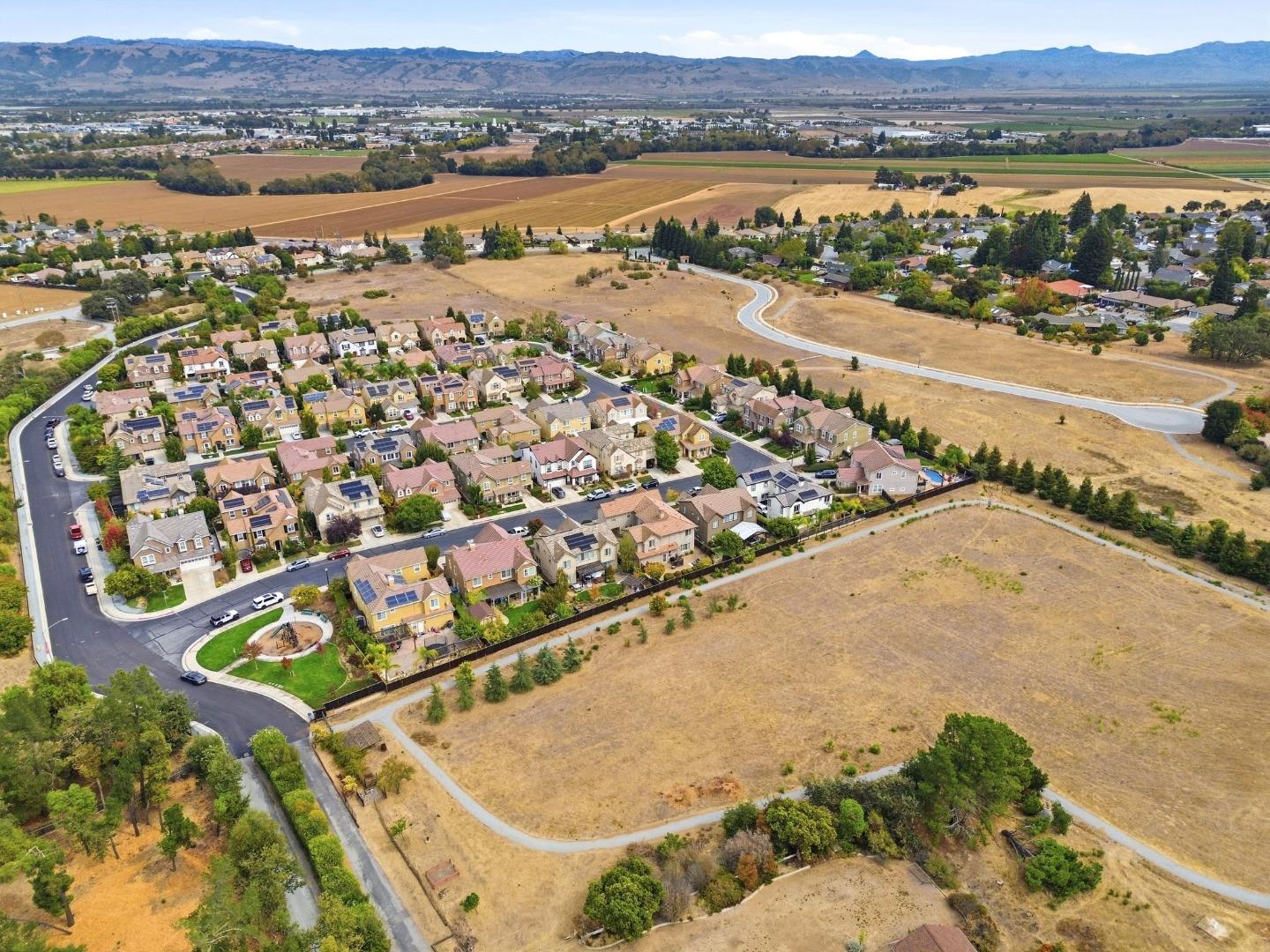 Aerial view of a neighborhood beside dry open fields, with farmland and mountains in the distance.