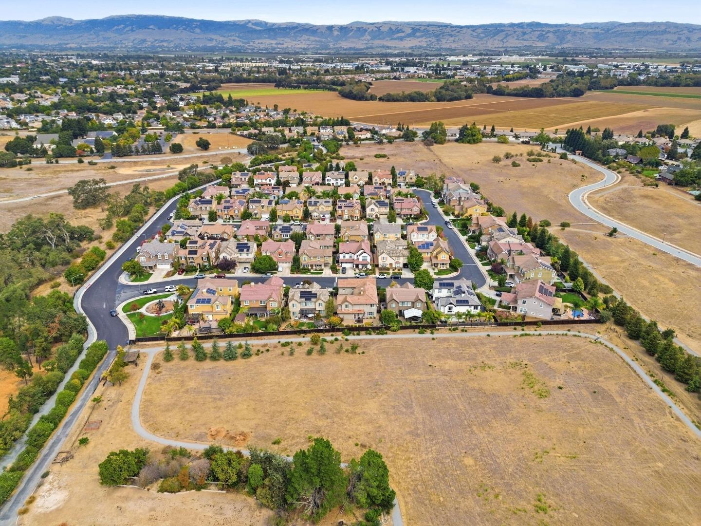 Aerial view of a residential neighborhood bordered by dry fields, with mountains in the distance.