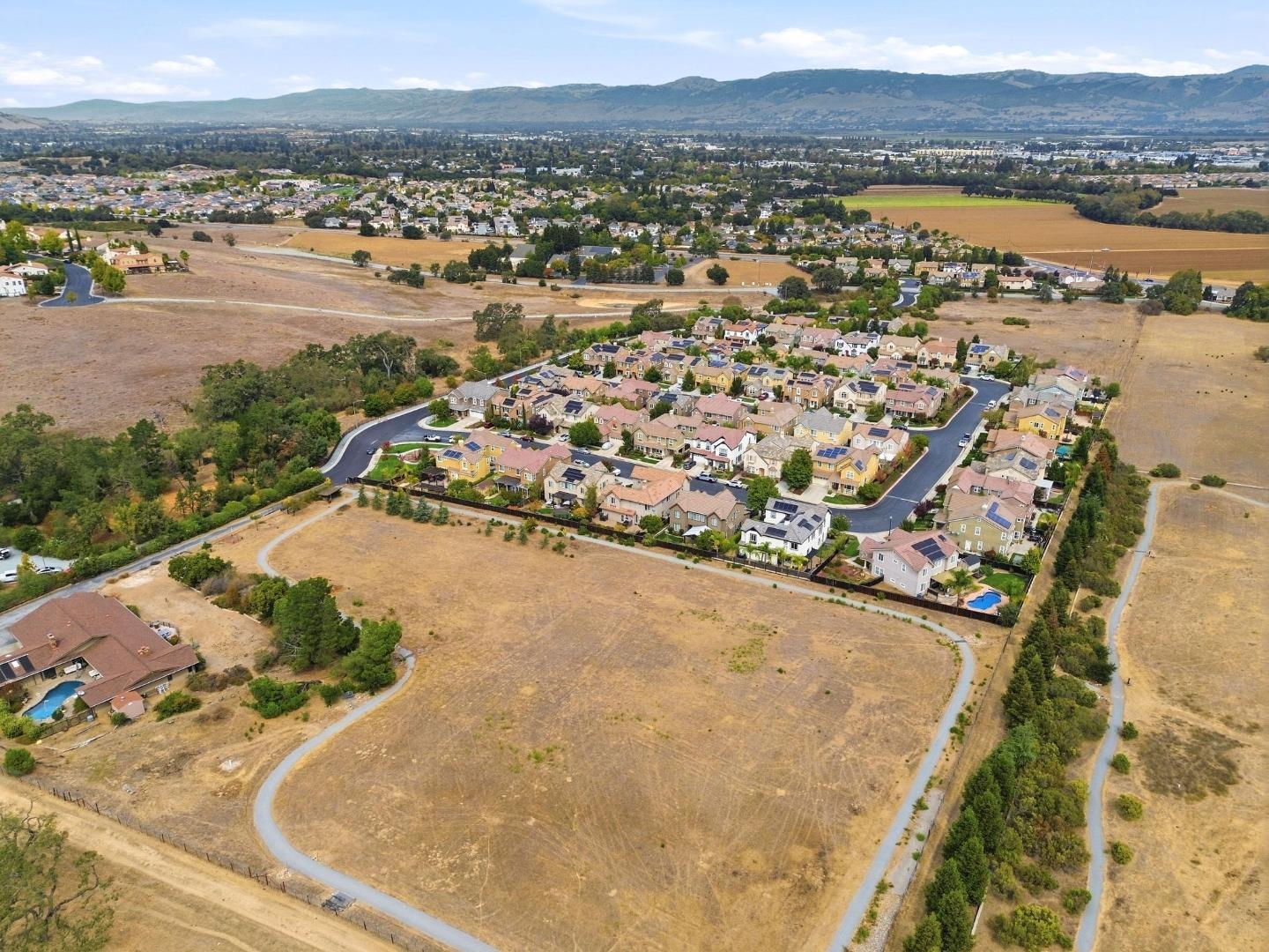 Aerial view of a residential neighborhood bordered by open fields, with mountains in the distance.