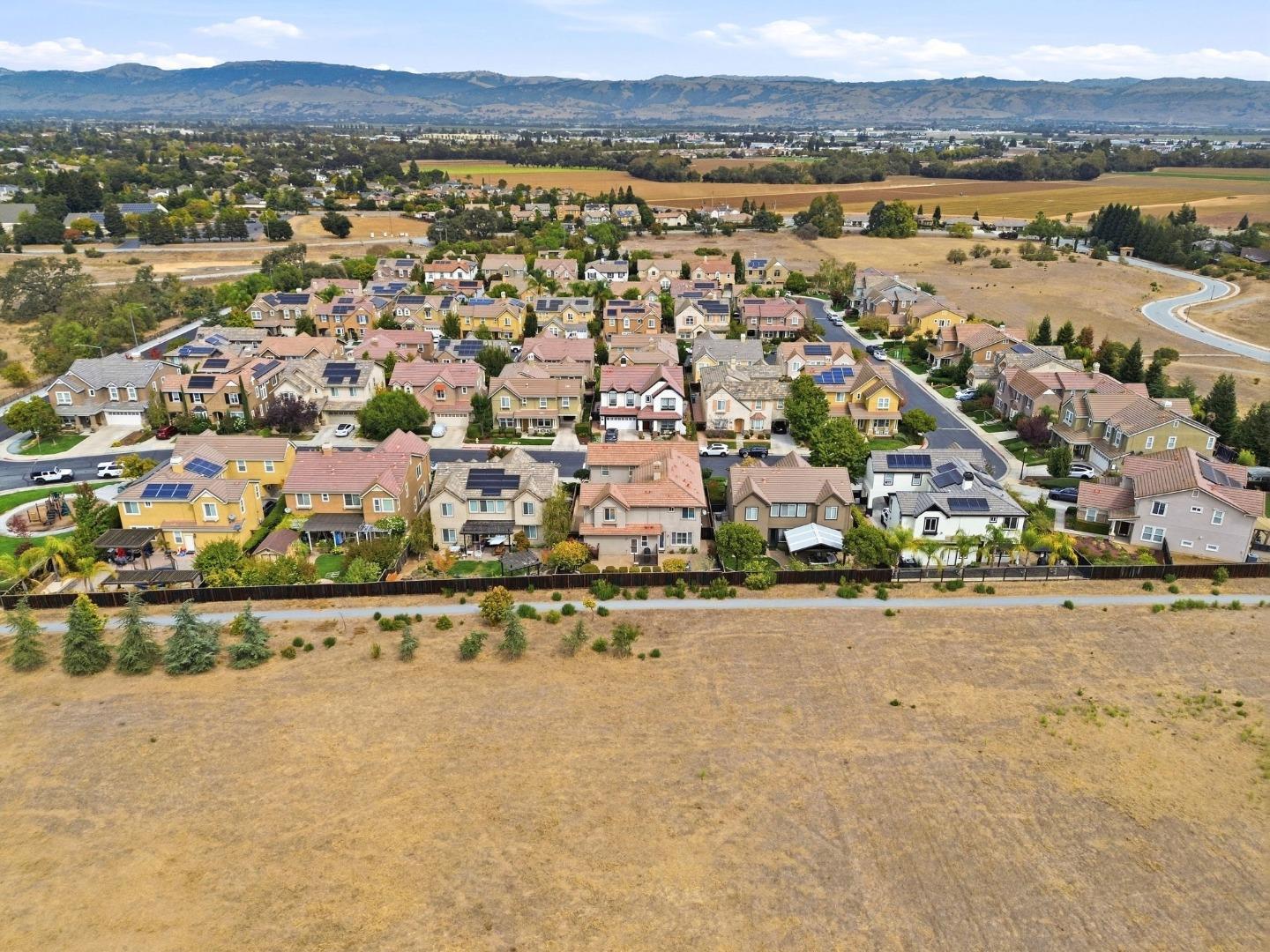 Aerial view of homes with solar panels, dry fields, and mountains in the distance.