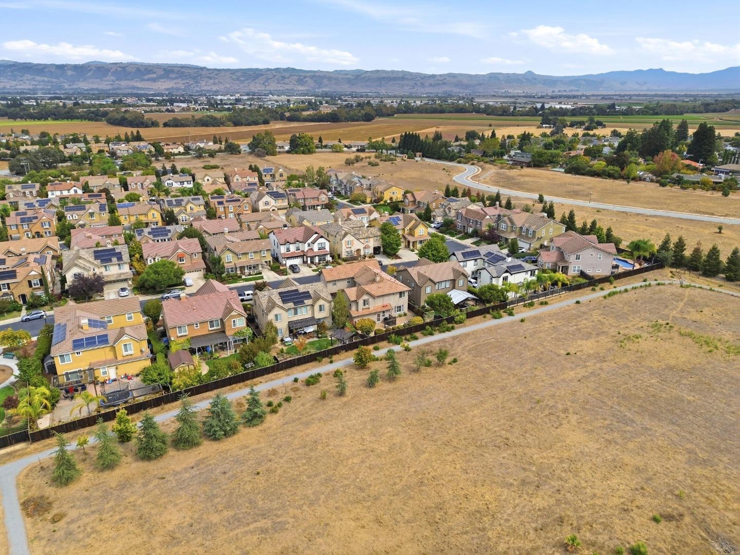 Aerial view of a Gilroy neighborhood beside an open lot, with farmland and mountains beyond.