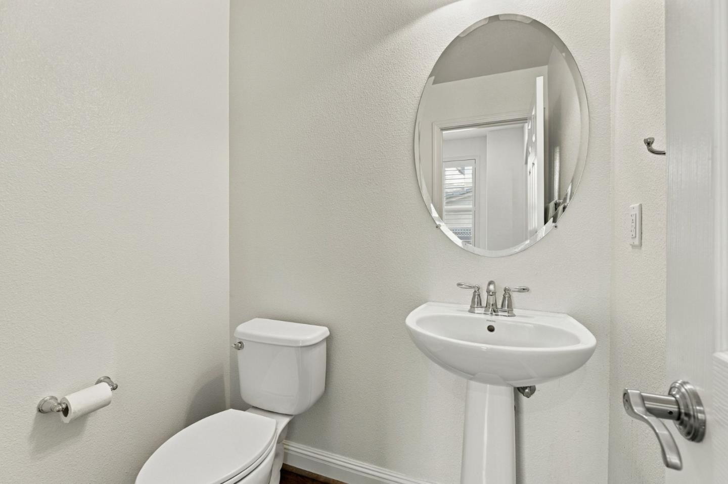 Bathroom with a pedestal sink, oval mirror, and white toilet.