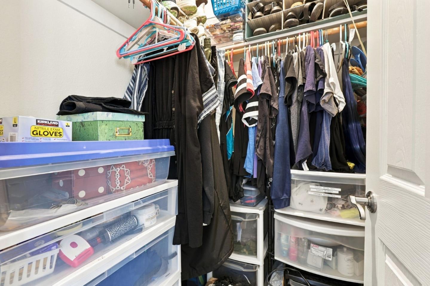 Closet packed with hanging clothes, shoes, and clear plastic storage drawers.