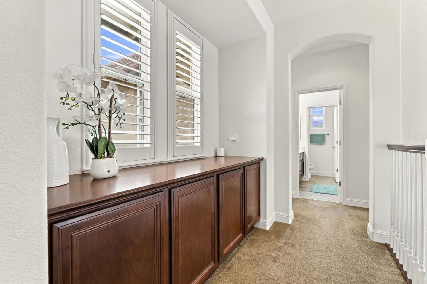 Upstairs hallway with a dark wood built-in cabinet, shuttered windows, and an arched bathroom doorway.