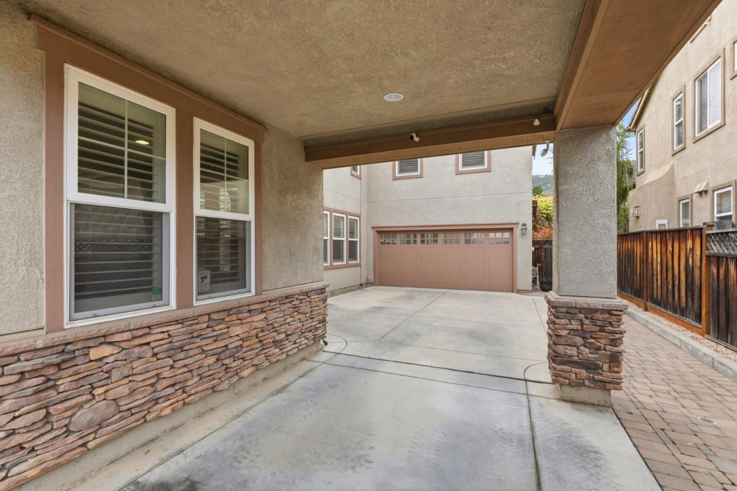 Covered driveway leading to a garage, with stone veneer walls and a paved side walkway.