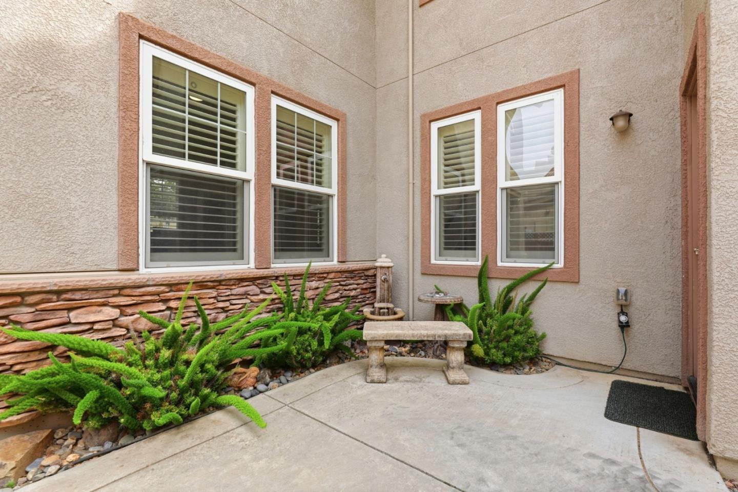 Courtyard patio with a stone bench, leafy planting beds, and shuttered windows.