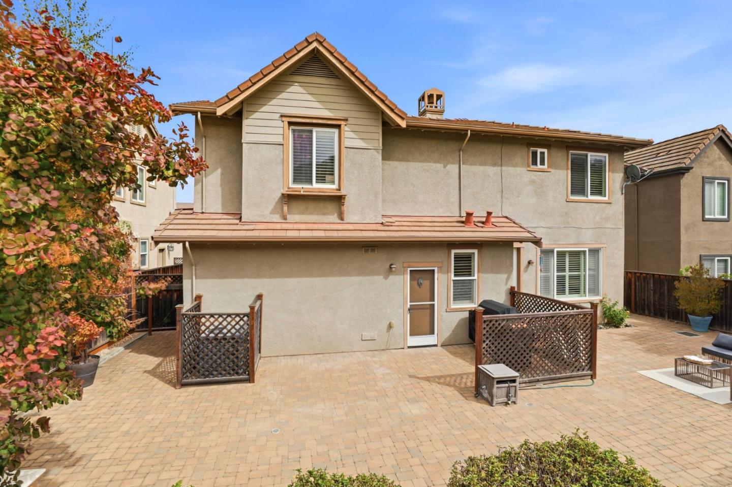 Home’s rear patio with broad paver courtyard, lattice screens, and outdoor seating.