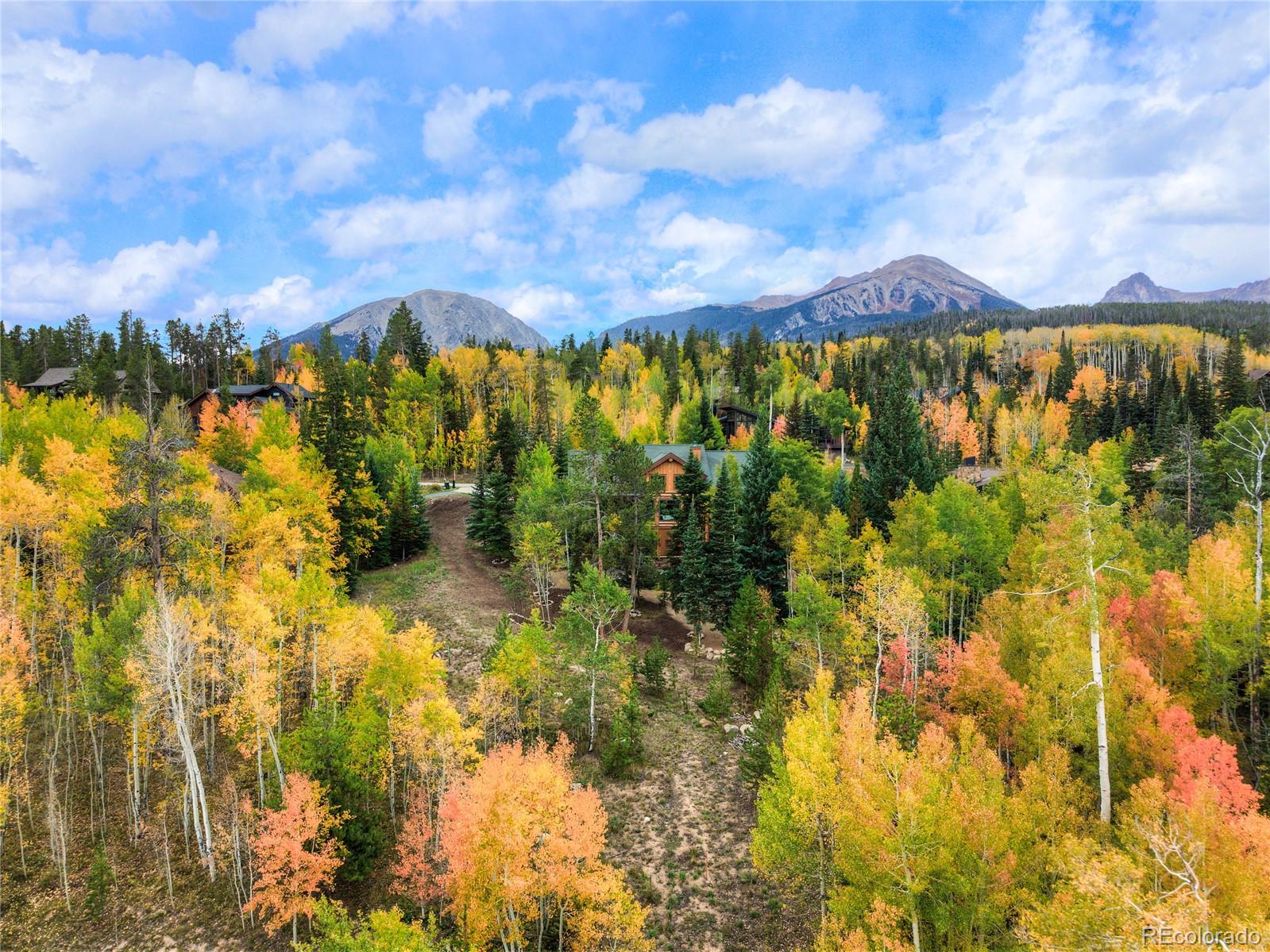 Aerial view of a mountain property clearing surrounded by autumn trees, with homes and mountain ridges beyond.