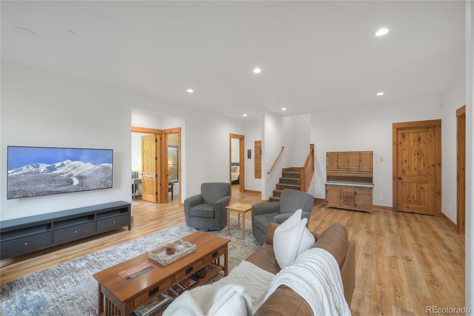 Furnished living room with hardwood floors, wood-trimmed doorways, and a staircase.