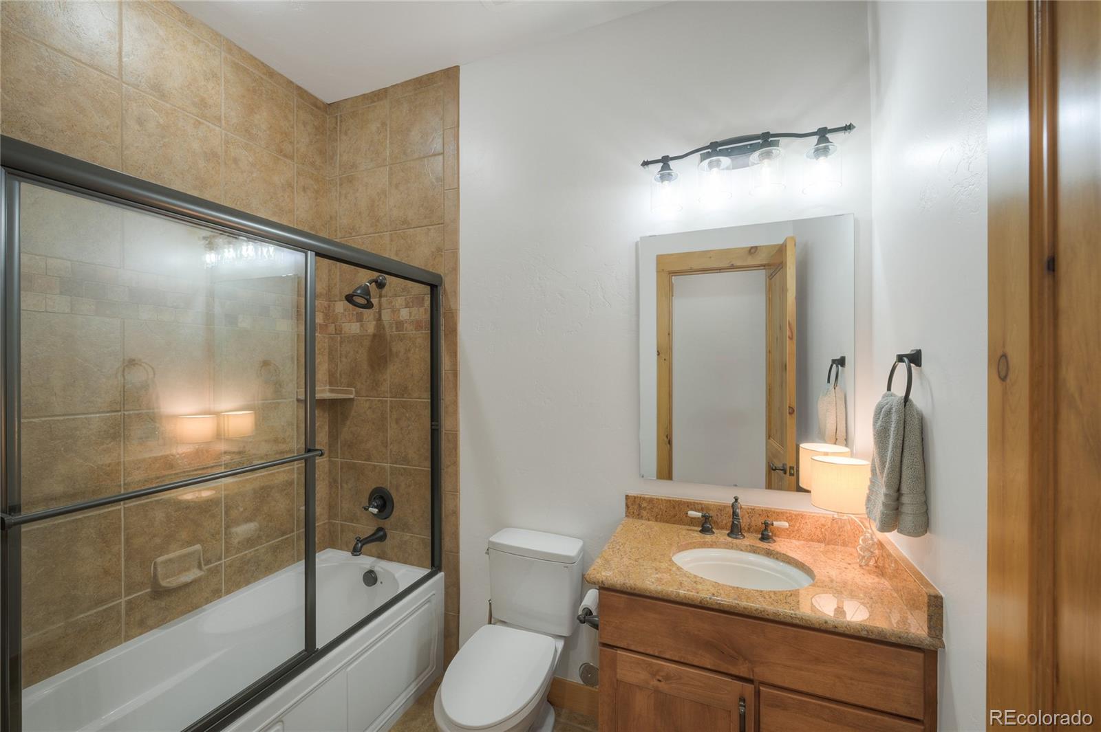 Bathroom with a tan tiled tub-shower, granite vanity, and wood cabinetry.