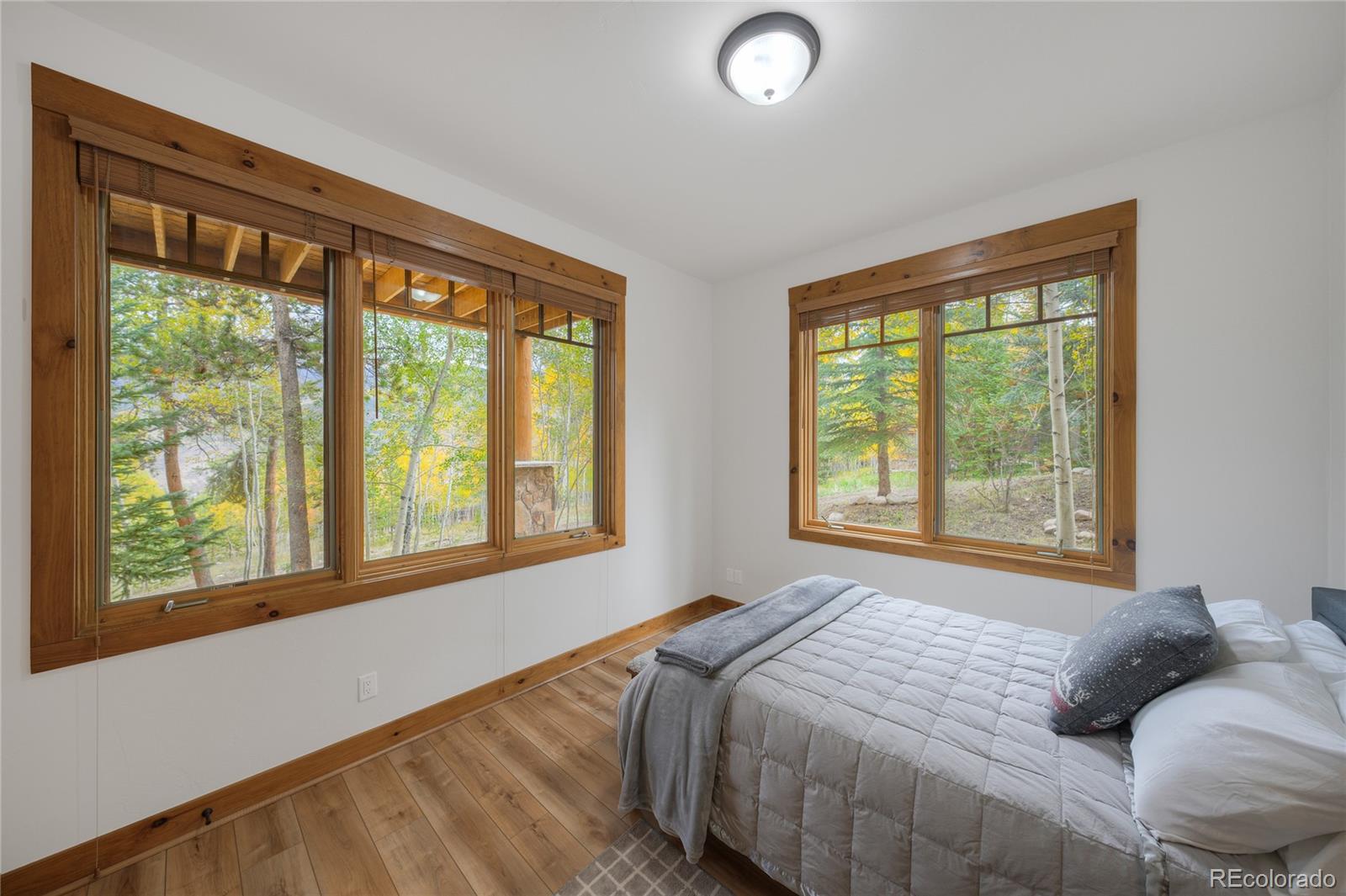Bedroom with broad wood-trimmed windows overlooking autumn trees.