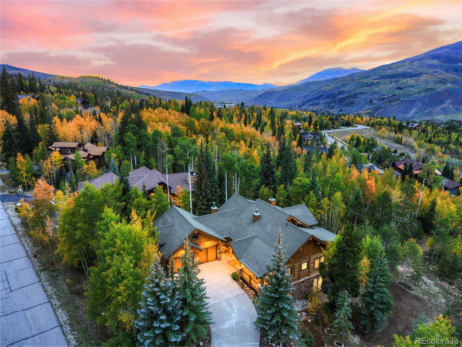 Mountain home among autumn trees, with a curved driveway and mountain ranges at sunset.