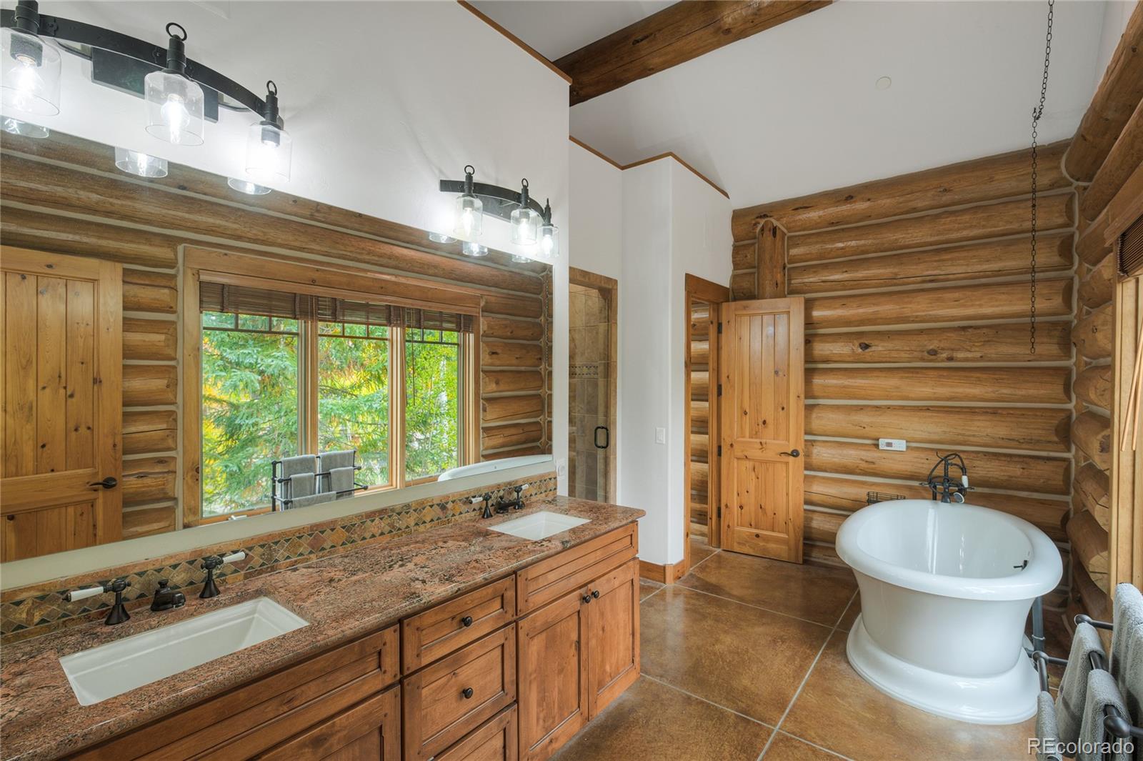 Rustic log-home bathroom with a double-sink wood vanity and freestanding soaking tub.