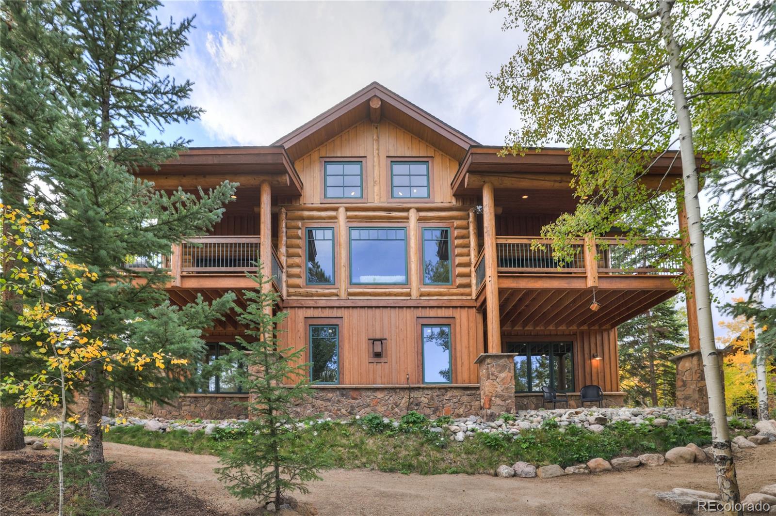 Log cabin home with broad upper balconies, a stone foundation, and wooded landscaping.