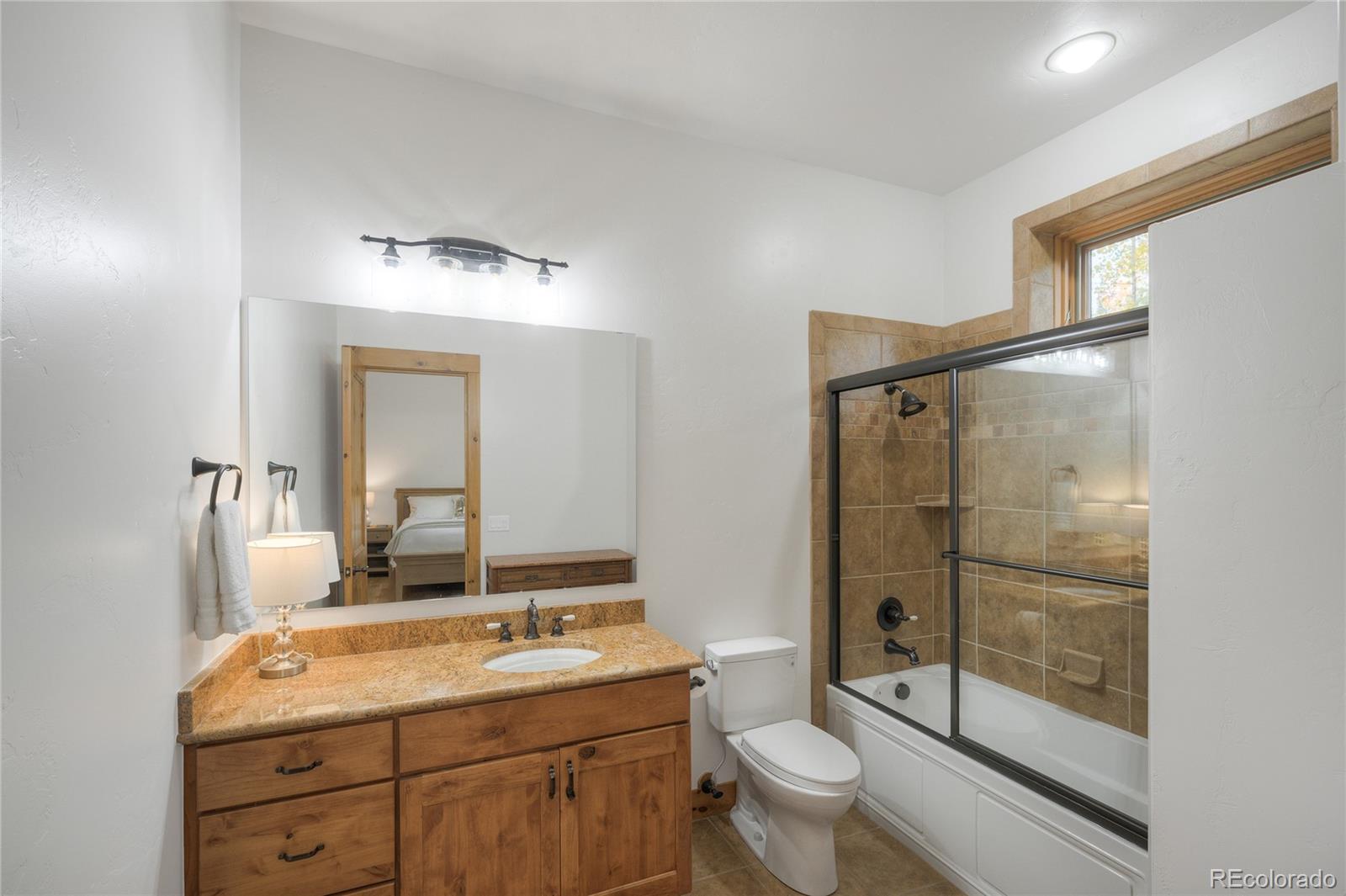 Bathroom with a wood vanity and stone countertop beside a glass-enclosed tan tile tub and shower.