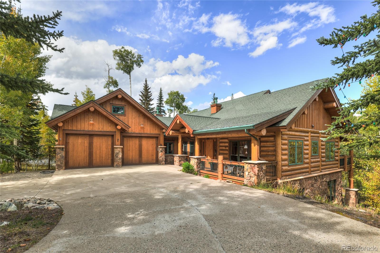 Rustic log home with a two-car garage, stone accents, and a broad driveway among trees.