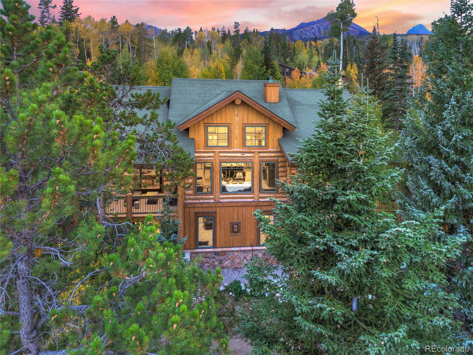 Log-style mountain home nestled among autumn trees, with a deck and mountain views at sunset.