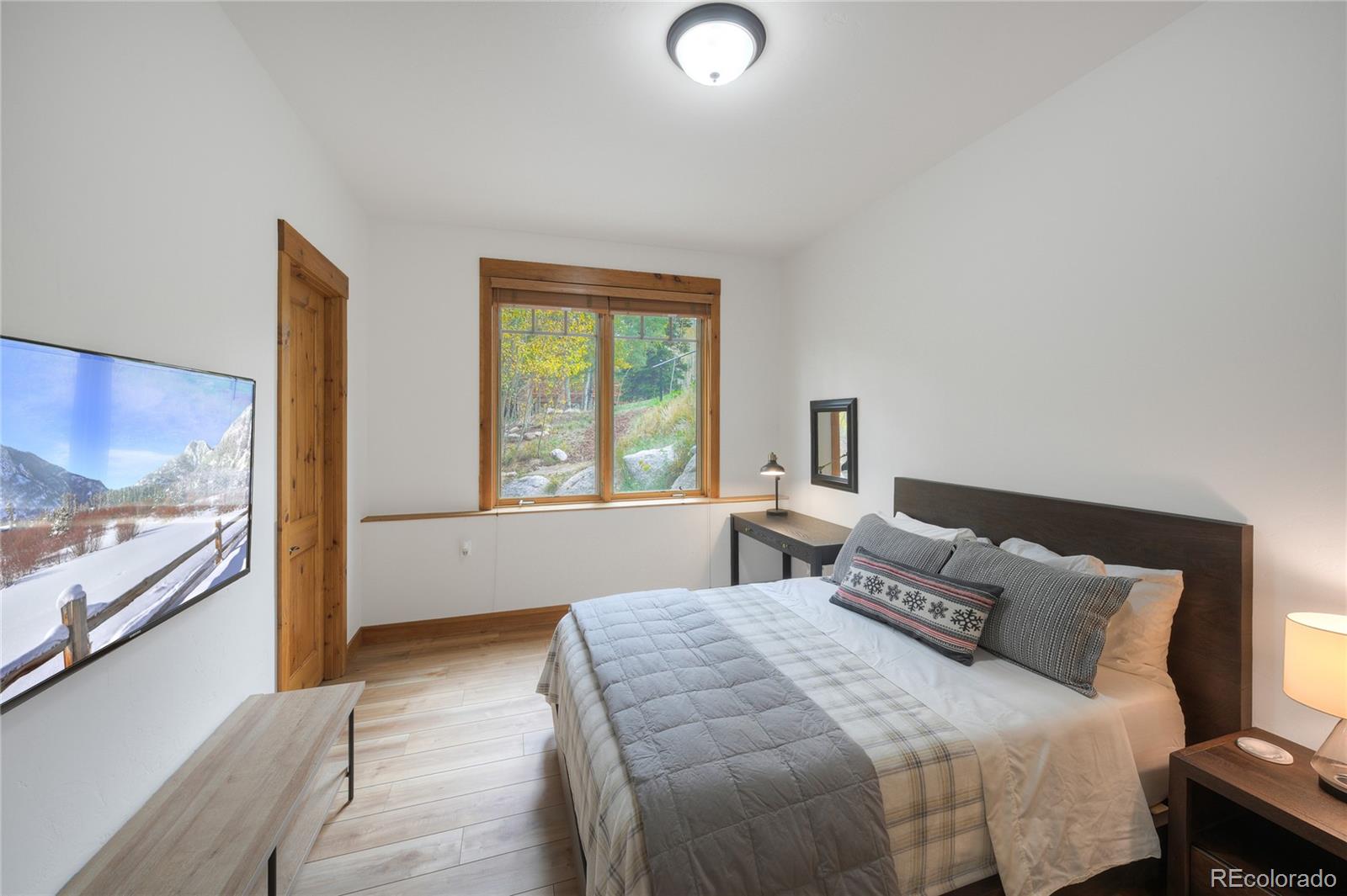 Furnished bedroom with a large bed, wood trim, and a window overlooking autumn foliage.