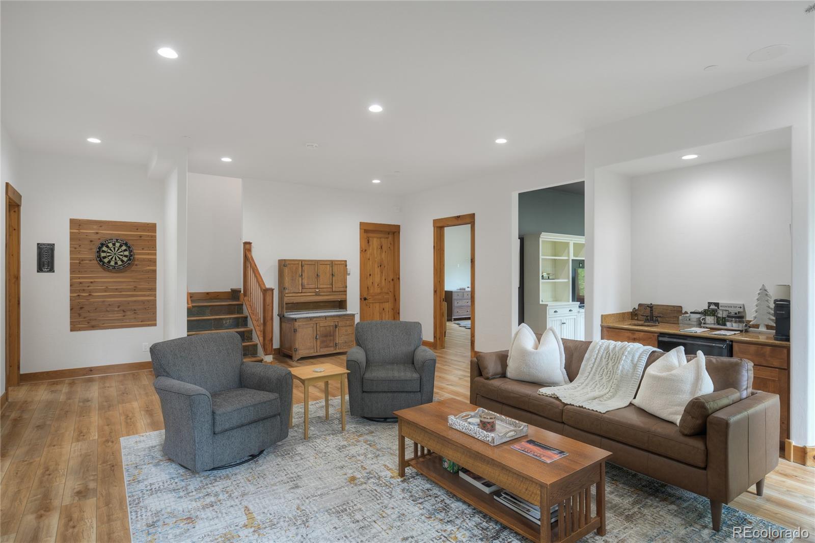 Furnished living room with leather sofa, gray armchairs, wood floors, and a dartboard wall.