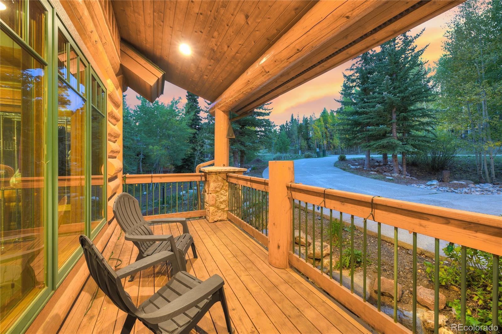 Covered wooden deck with Adirondack chairs overlooking trees and a curving driveway.