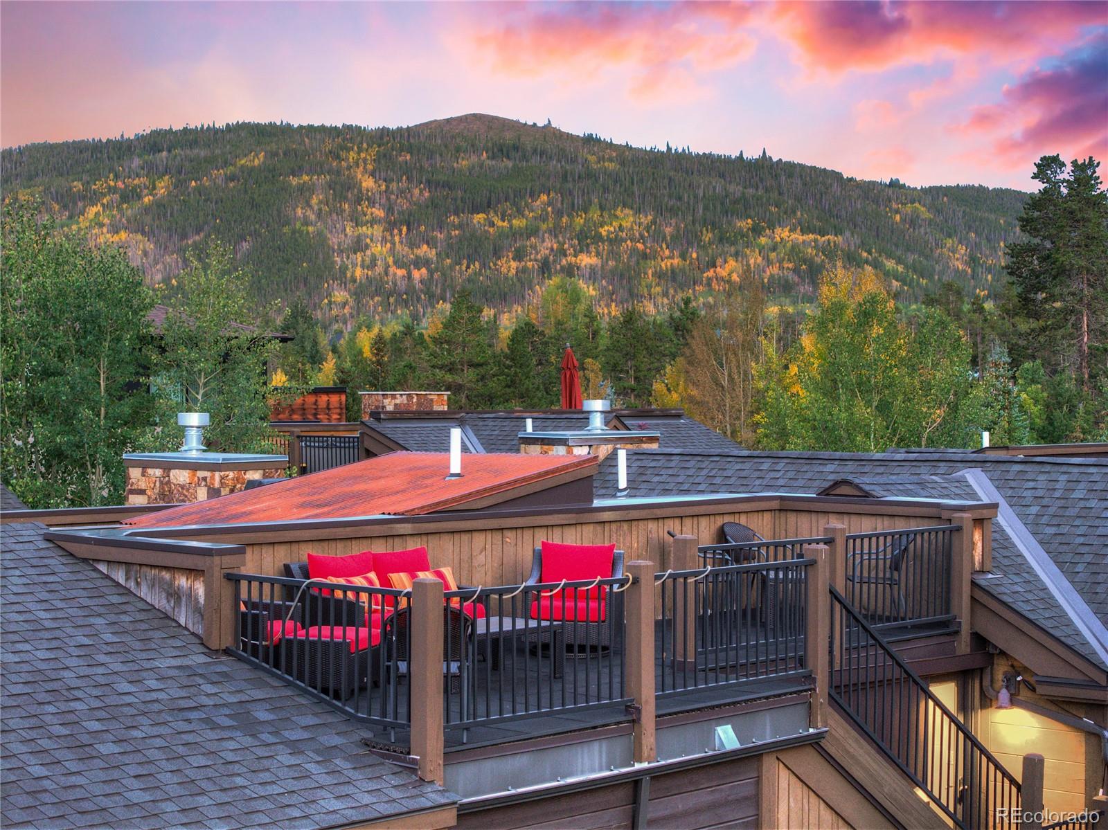 Rooftop deck with red-cushioned seating and a forested mountain view at sunset.