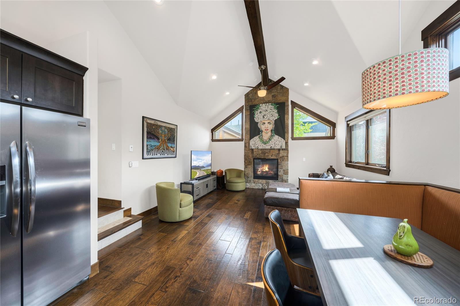 Open-plan living and dining area with vaulted ceiling, stone fireplace, and dark wood floors.