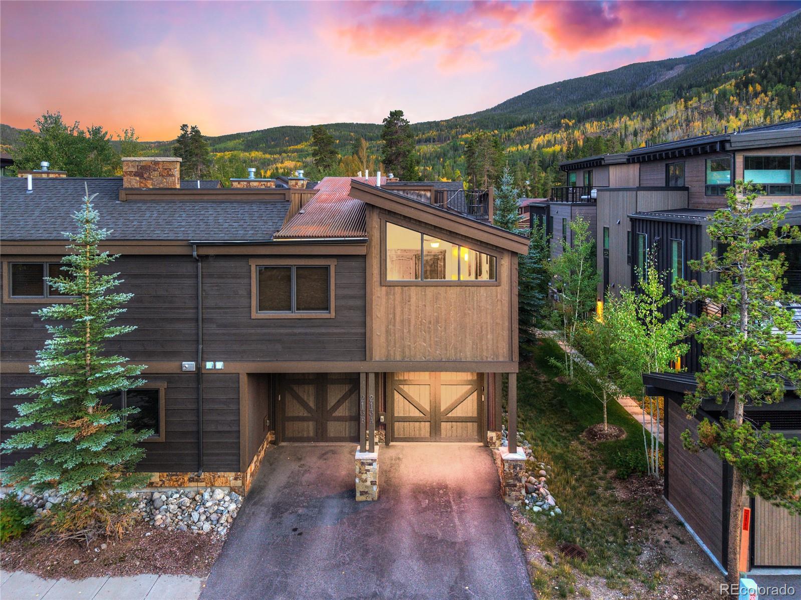 Townhome exterior with a mountain backdrop, twin garage doors, and autumn aspens at sunset.