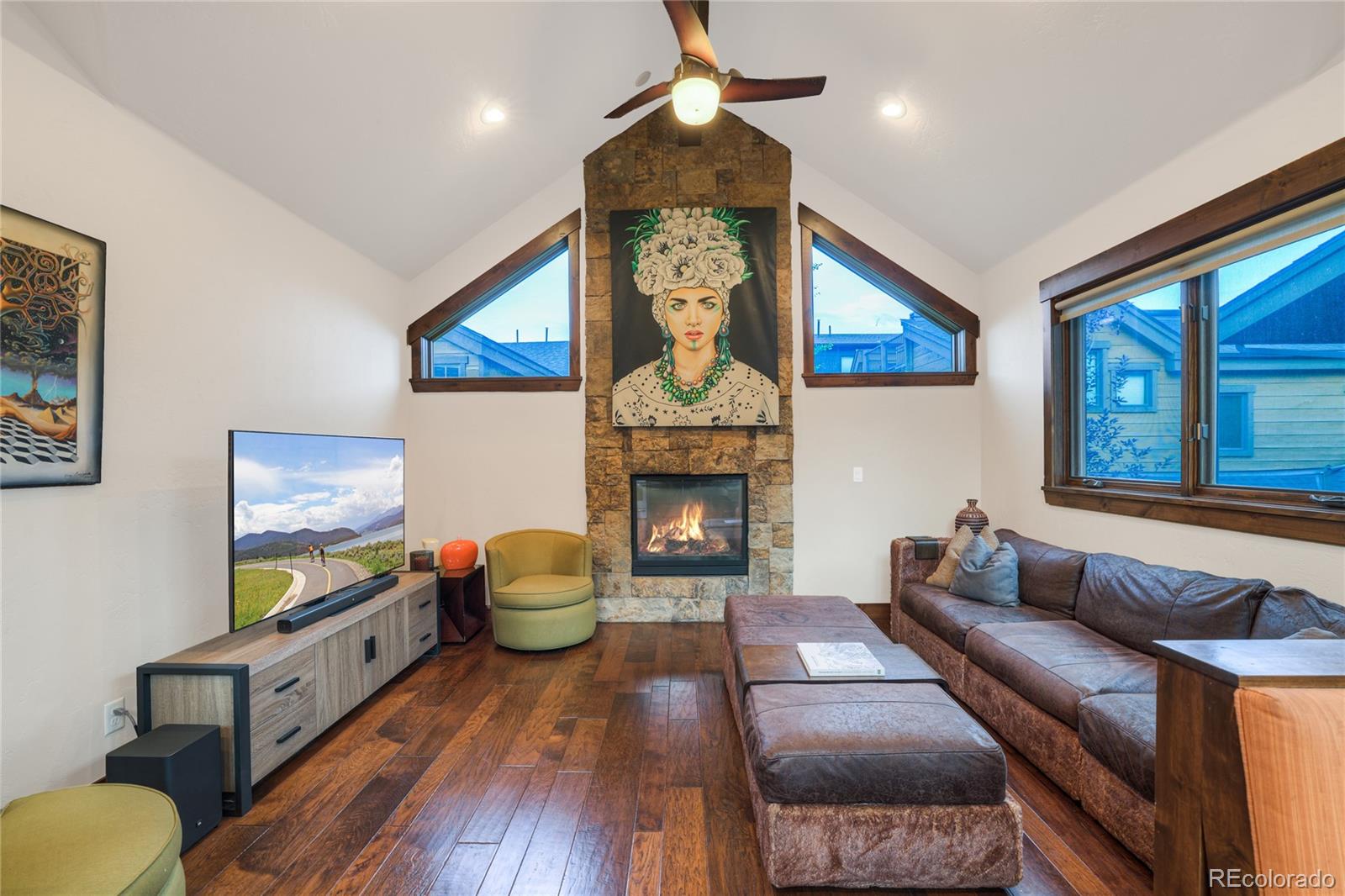 Living room with a stone fireplace, vaulted ceiling, hardwood floors, and leather sectional.