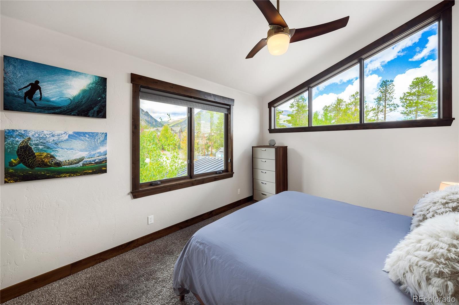 Bedroom with large mountain-view windows, a ceiling fan, and ocean-themed wall art.