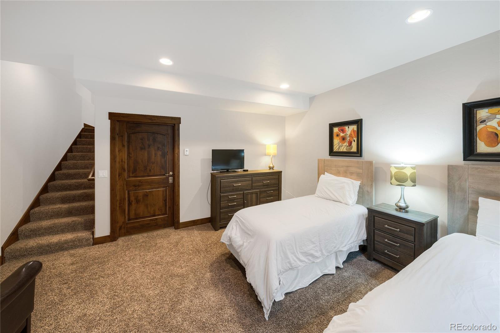 Bedroom with two single beds, brown carpet, and a staircase beside the entry door.