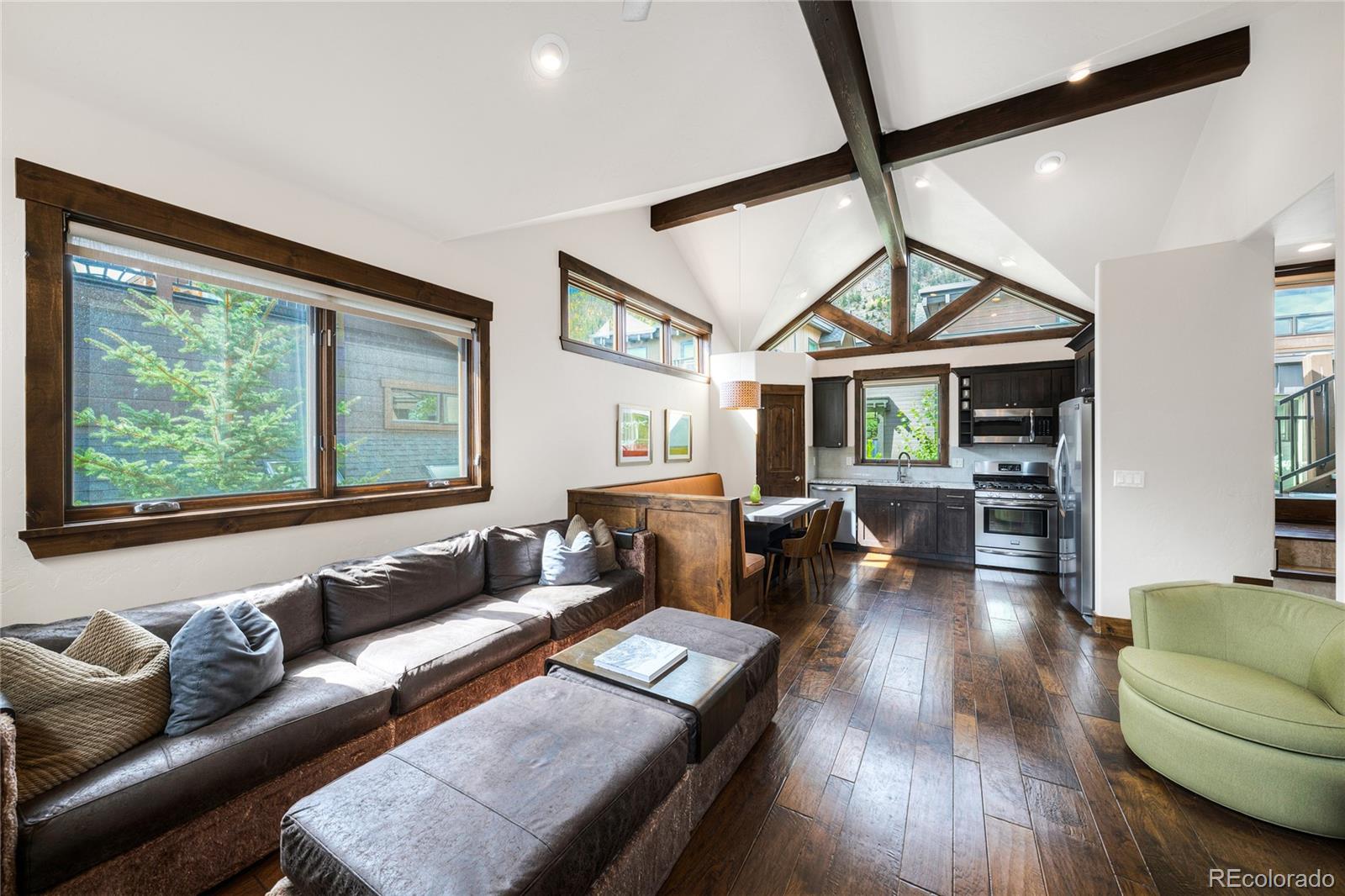 Open-plan living room and kitchen with vaulted ceilings, exposed beams, and large windows.