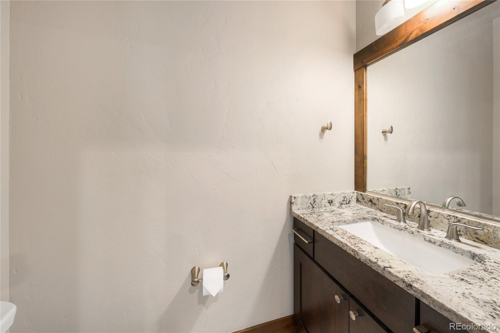 Bathroom vanity with a speckled stone countertop, dark wood cabinets, and a large mirror.