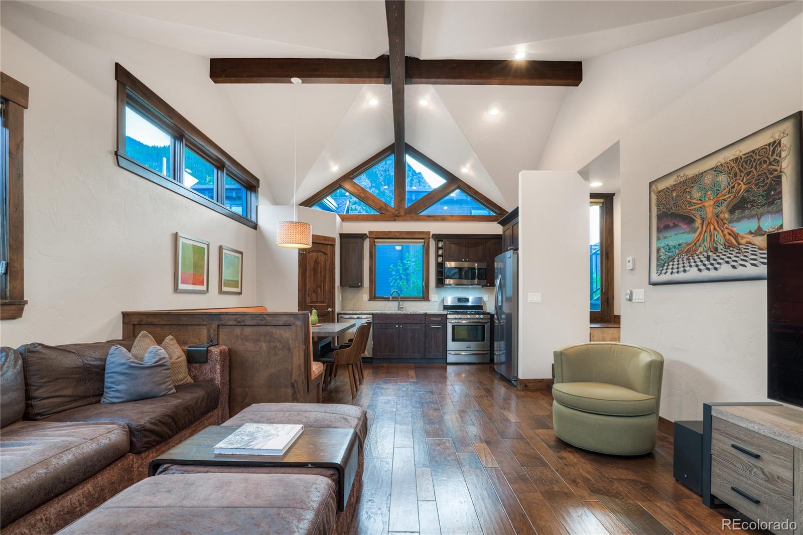 Open-plan living room and kitchen with vaulted ceilings, exposed beams, and mountain views through large windows.