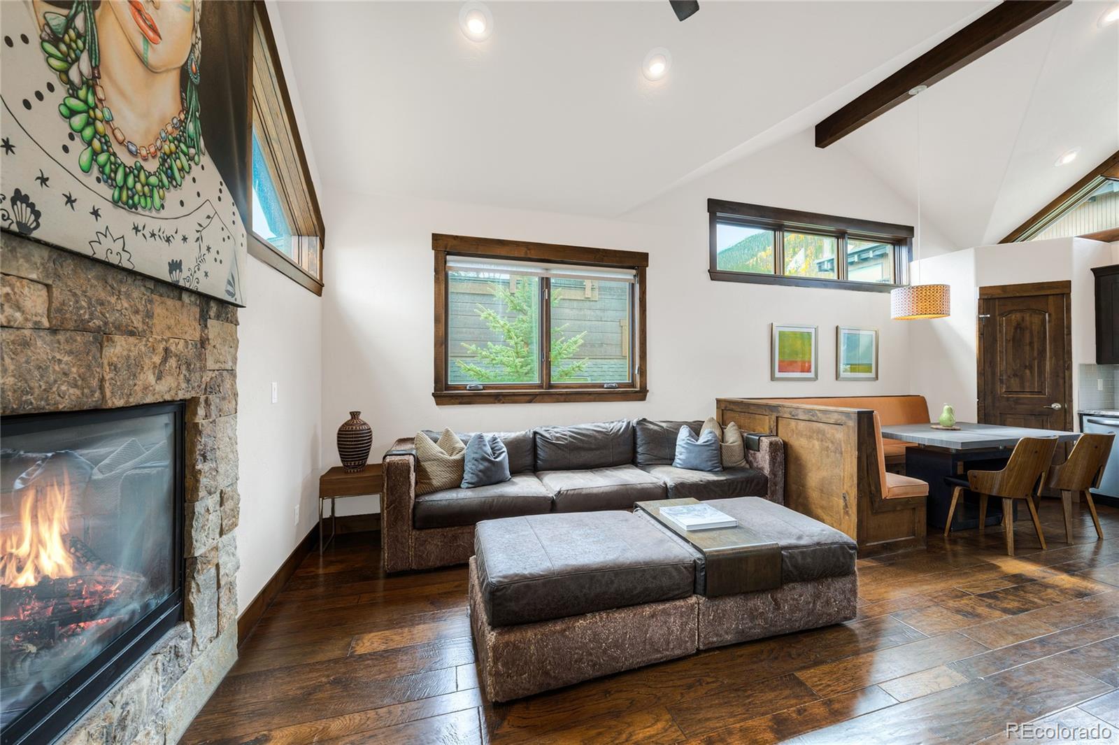 Living room with a stone fireplace, leather sectional, vaulted ceiling, and mountain views through the windows.