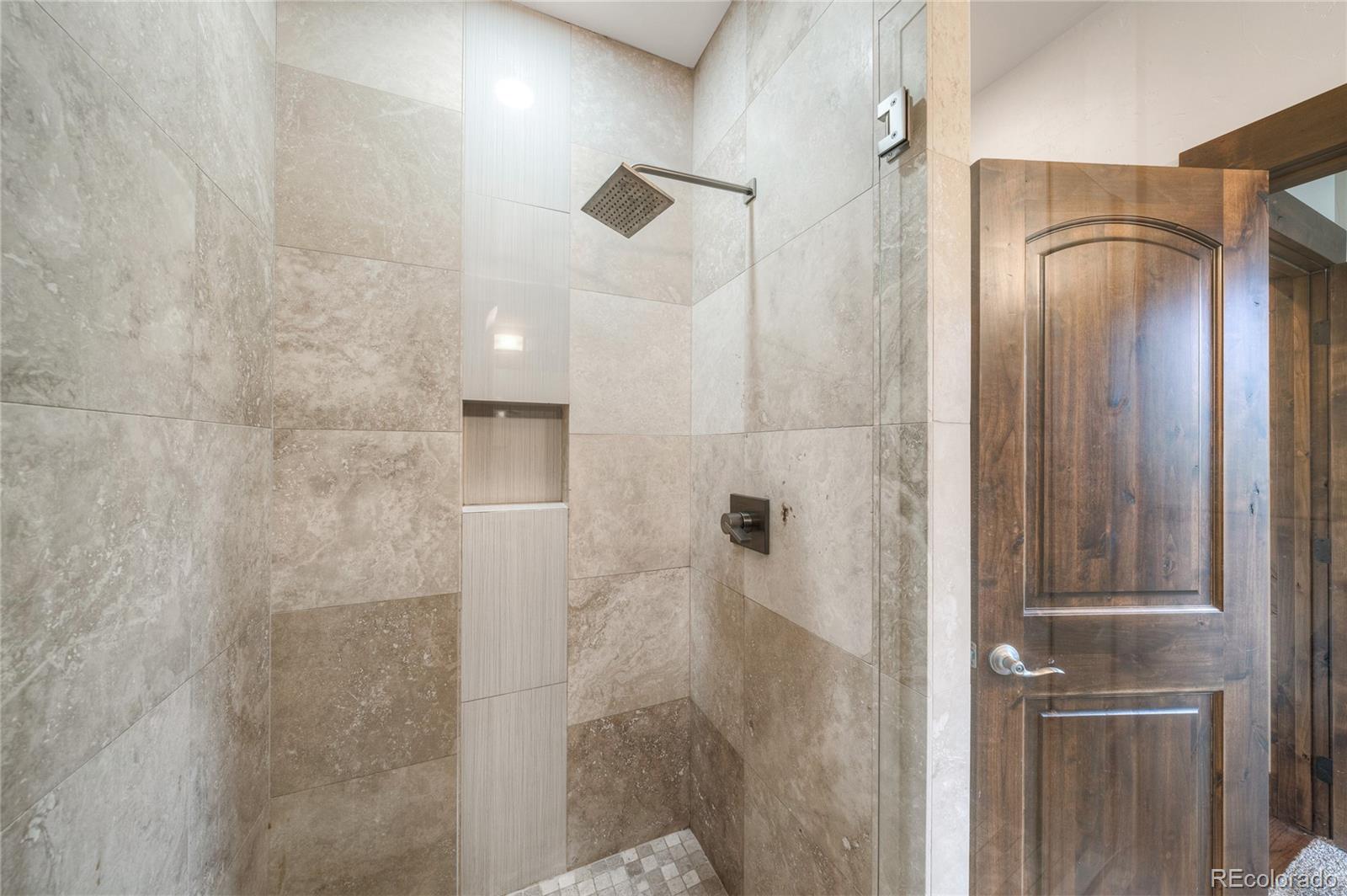 Walk-in shower with stone-look tile, a square rainfall showerhead, and a built-in niche.
