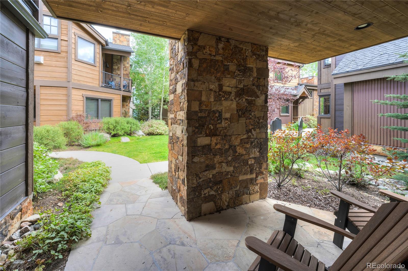 Covered flagstone patio with a stone pillar and wooden chairs in a landscaped townhouse courtyard.