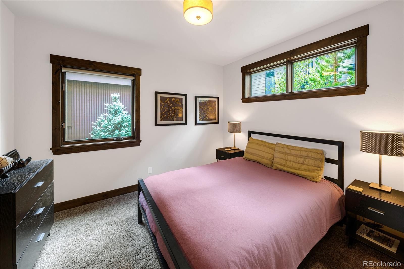 Furnished bedroom with a pink bedspread, dark wood trim, and two windows.