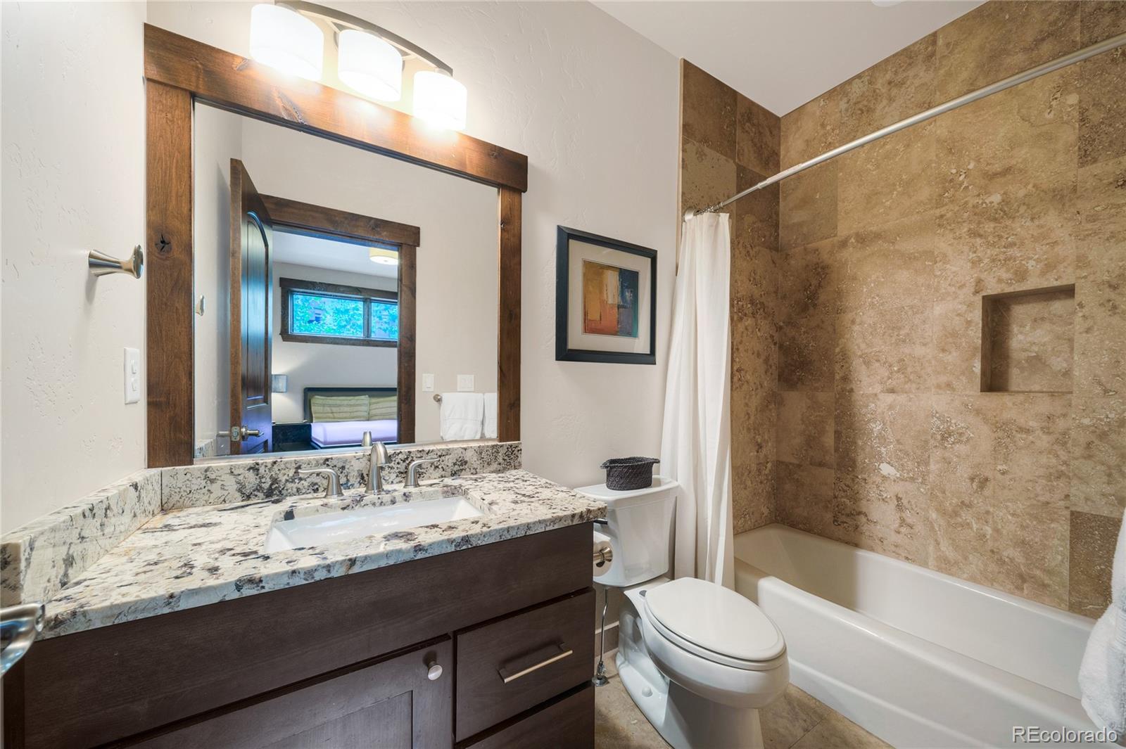 Bathroom with a granite vanity and a tan stone-tiled tub and shower.