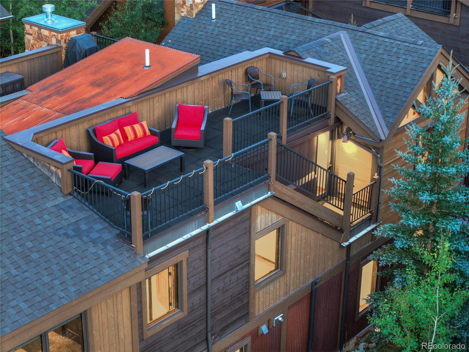 Rooftop deck with red-cushioned seating, black railings, and views of surrounding shingled roofs.