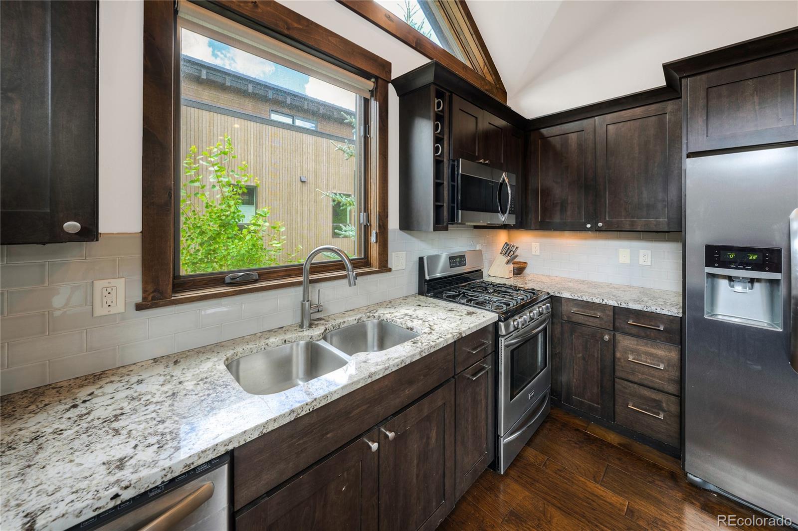Kitchen with dark wood cabinets, granite counters, a double sink, and stainless steel appliances.